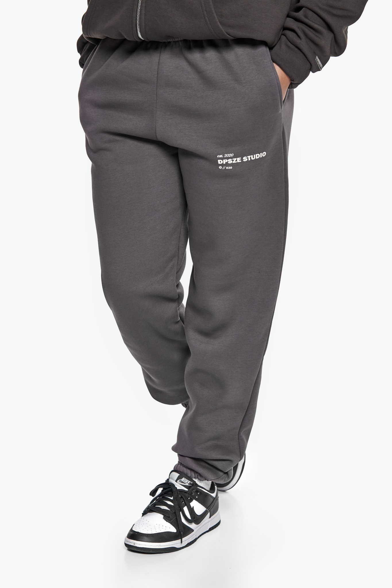 Graue Jogginghose von Dropsize mit seitlichem Logo-Print, kombiniert mit schwarzen Sneakern, Nahaufnahme.